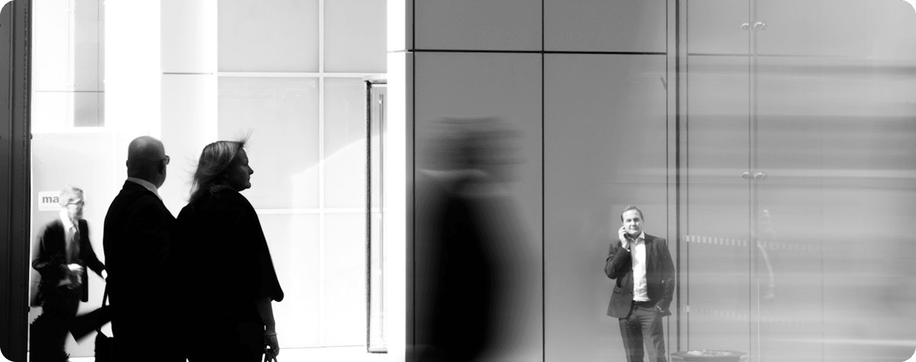 Black and white panoramic view of professionals in motion within a bright modern office with glass walls.