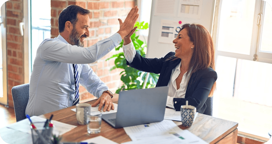 Two colleagues celebrating with a high-five across a desk.